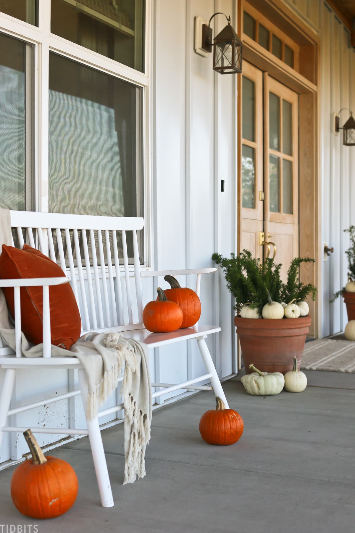 front porch decorated for fall with white and orange pumpkins plus a bench with pillow and blanket