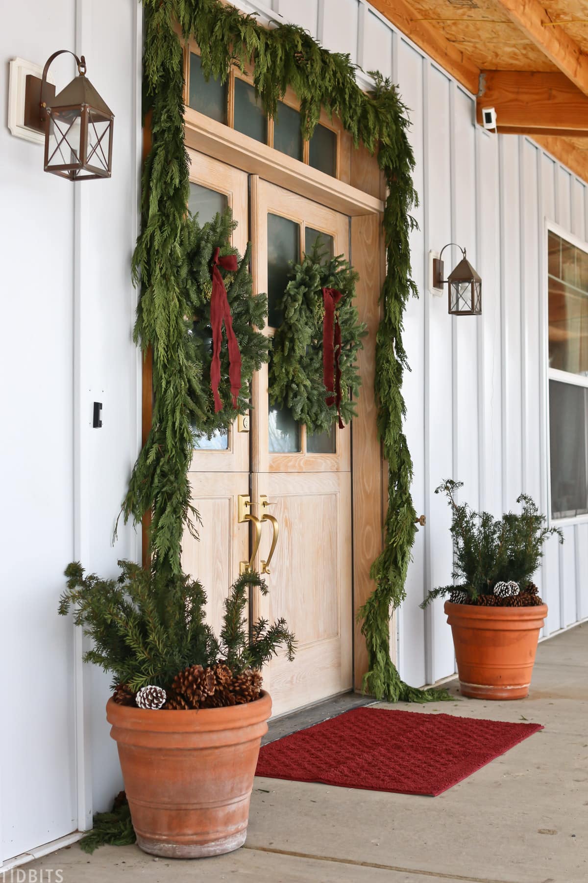 cedar garland and wreaths hang on a front door at christmas time.