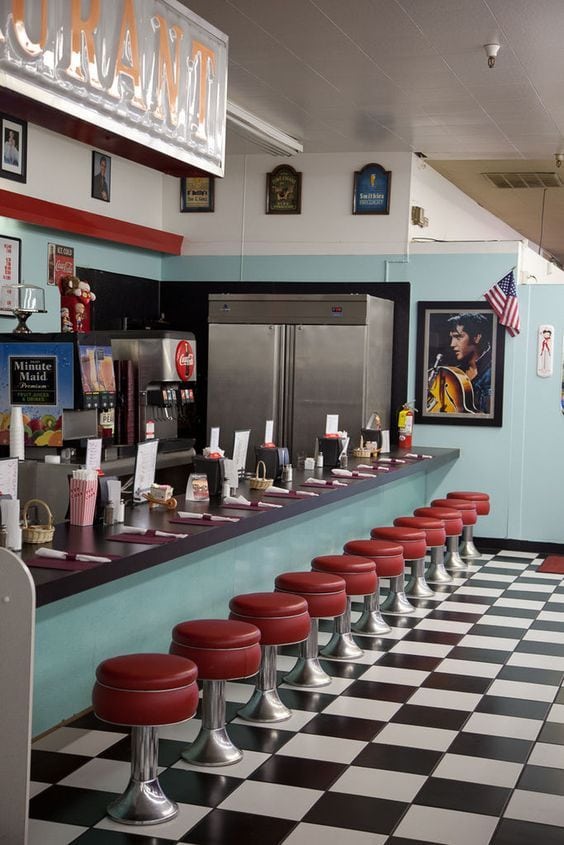 1950s diner with black and white floor tiles and red-rounded chairs in front of the booth