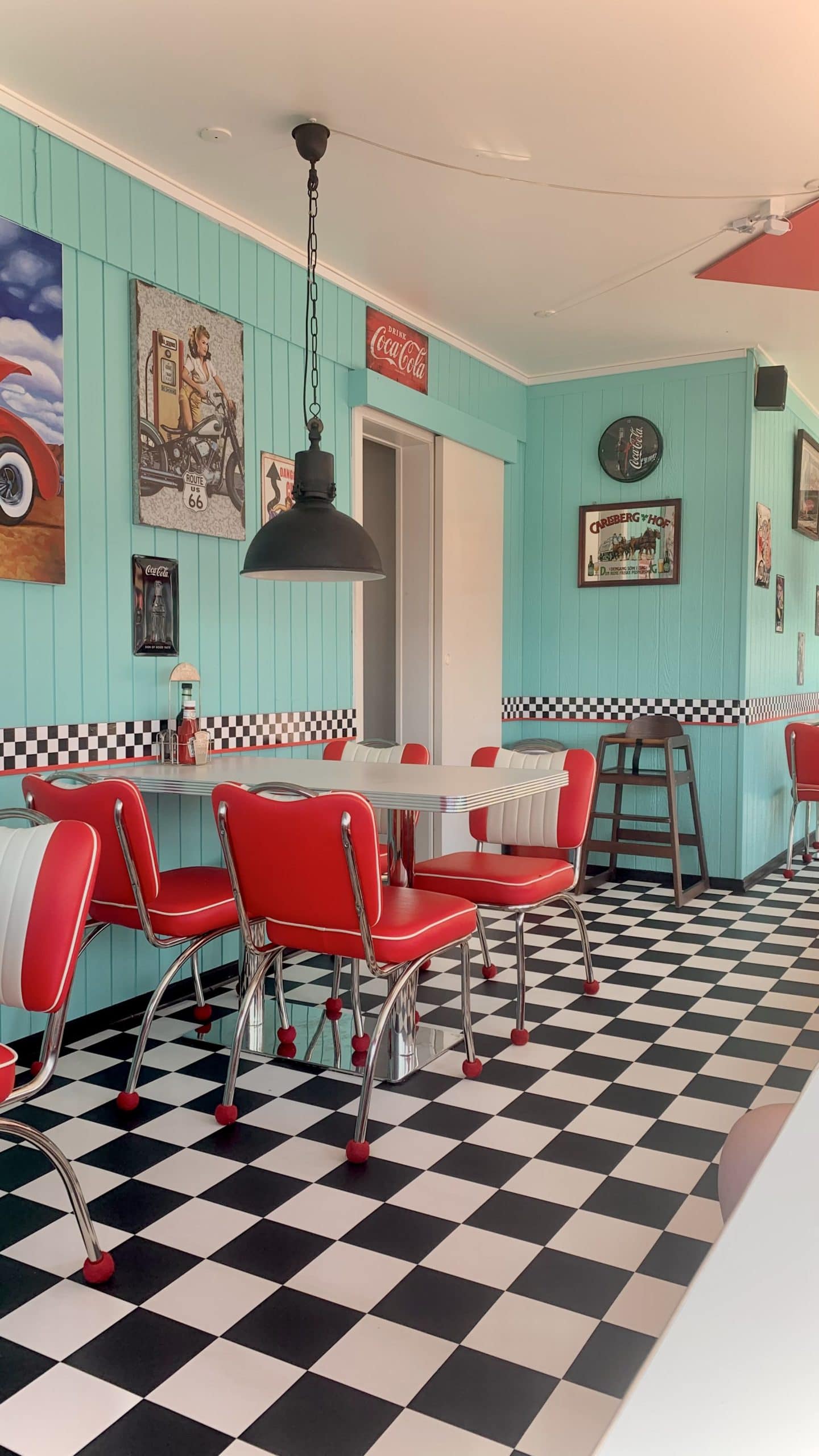 1950s diner with black and white floor tiles, red chairs, white tables, and blue wall