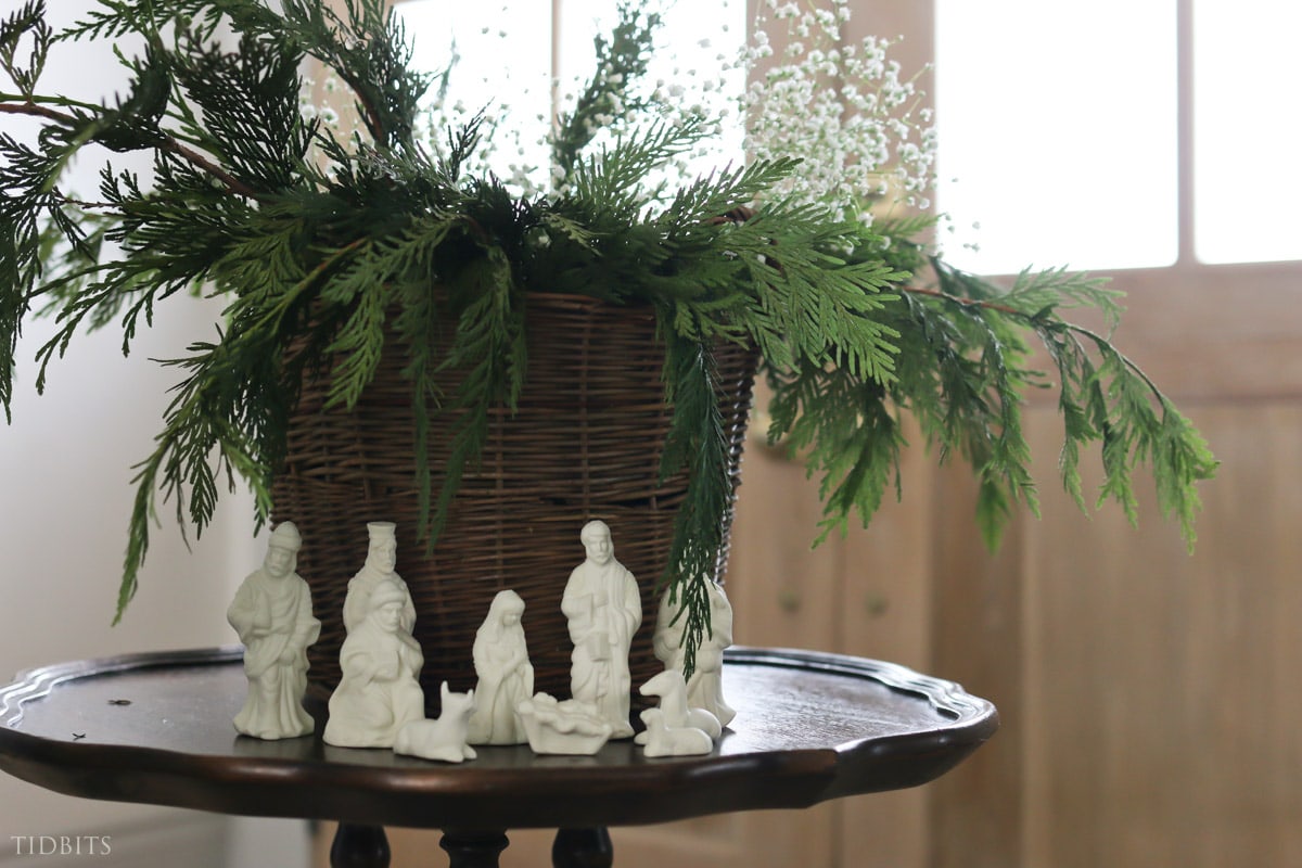 porcelain nativity set sitting under a basket full of greens