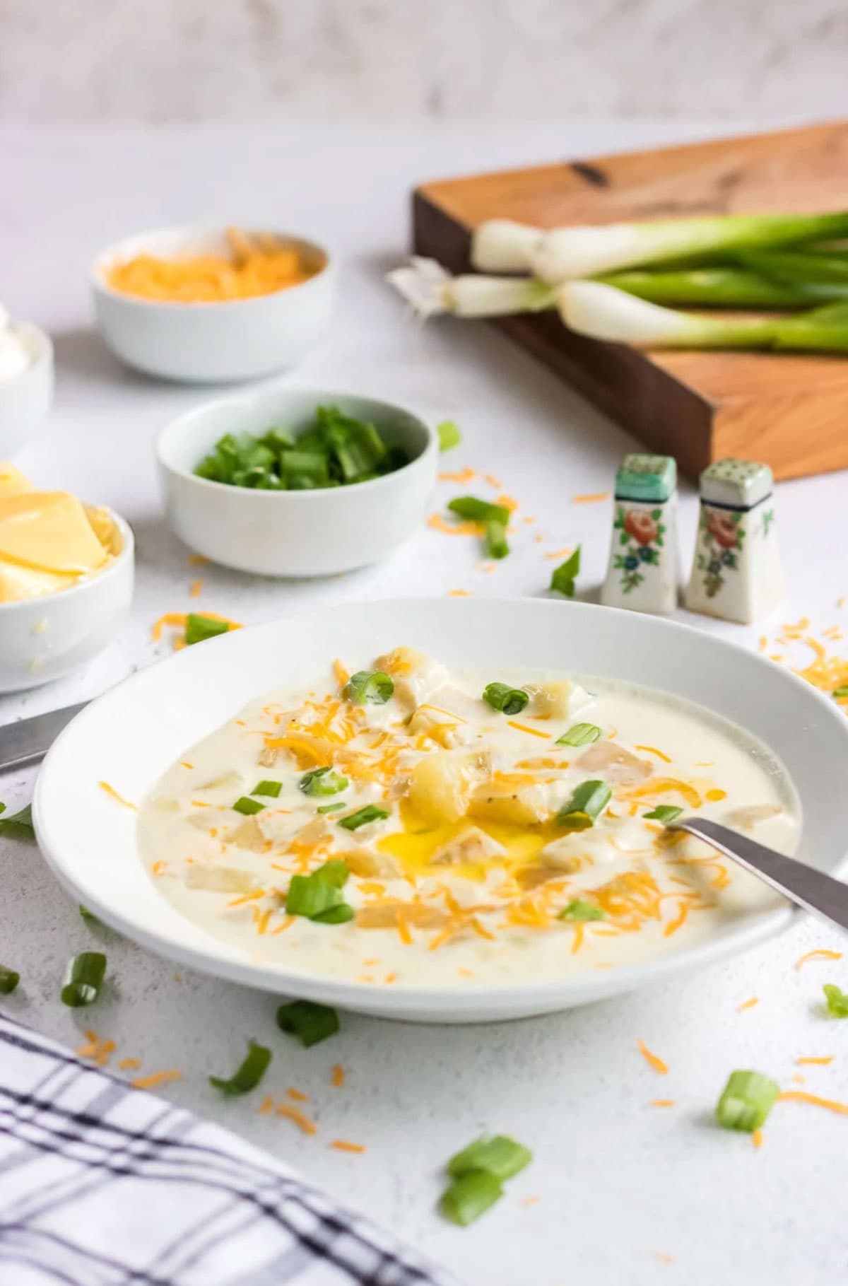 A bowl of old fashioned potato soup on a table with toppings 