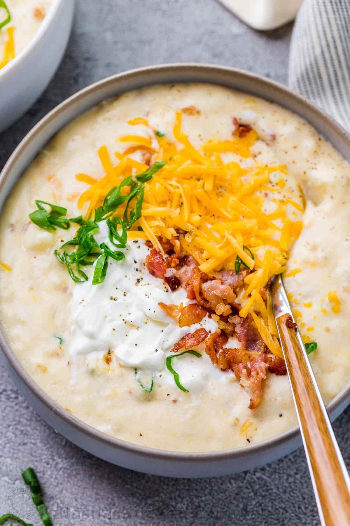 Bowl of loaded potato soup with green onion, sour cream, bacon and cheddar cheese