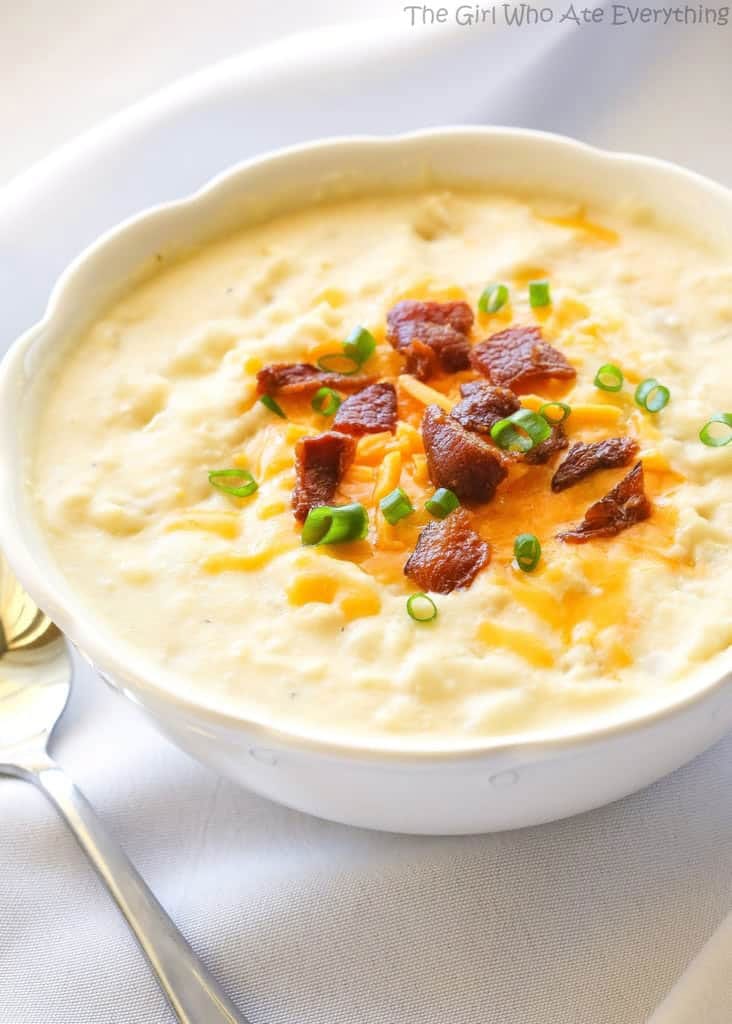 White bowl full of creamy potato soup garnished with cheddar cheese, green onions and bacon pieces
