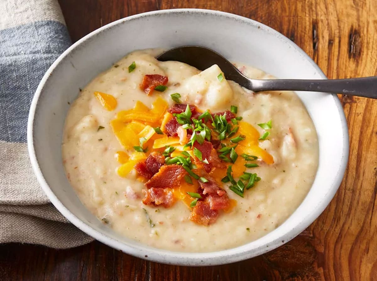 Spoon in a bowl of creamy and chunky potato soup with cheese, onions, and bacon on top