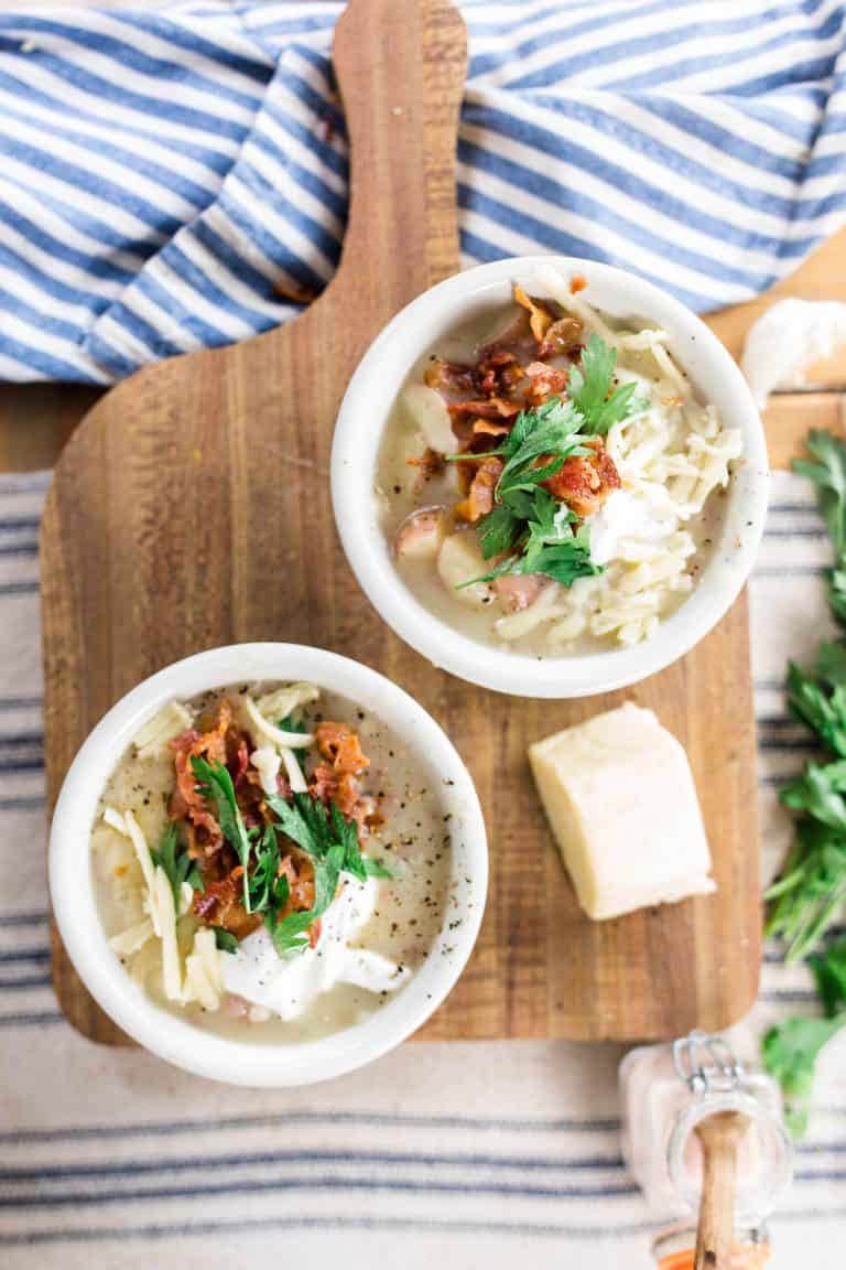 Two bowls of hearty potato soup with cheese, sour cream, bacon and herb toppings