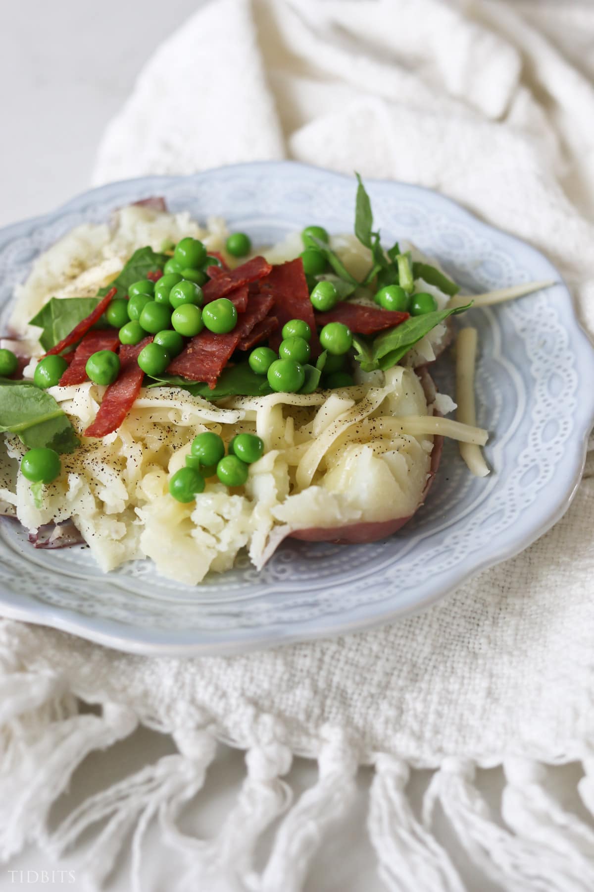 Quick and easy baked potato dinner topped with bacon, greens and peas