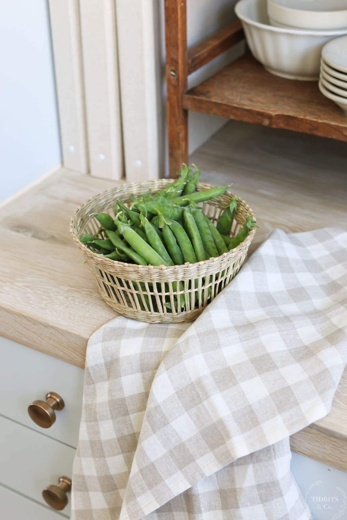 A bowl of peas and a linen tea towel sit on a butcher block countertop