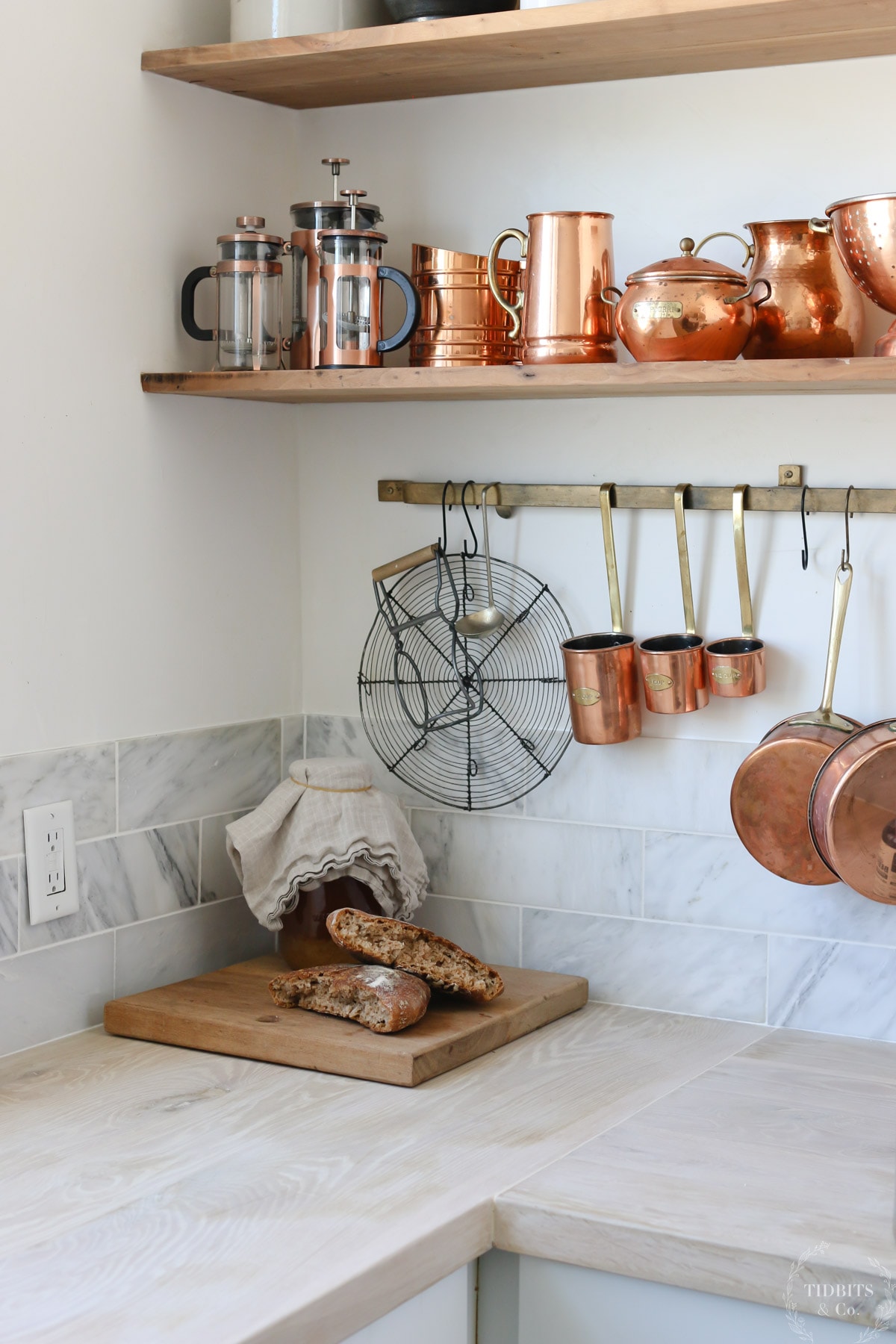 Copper pots and pans hang on a kitchen rack and sit on a wood shelf