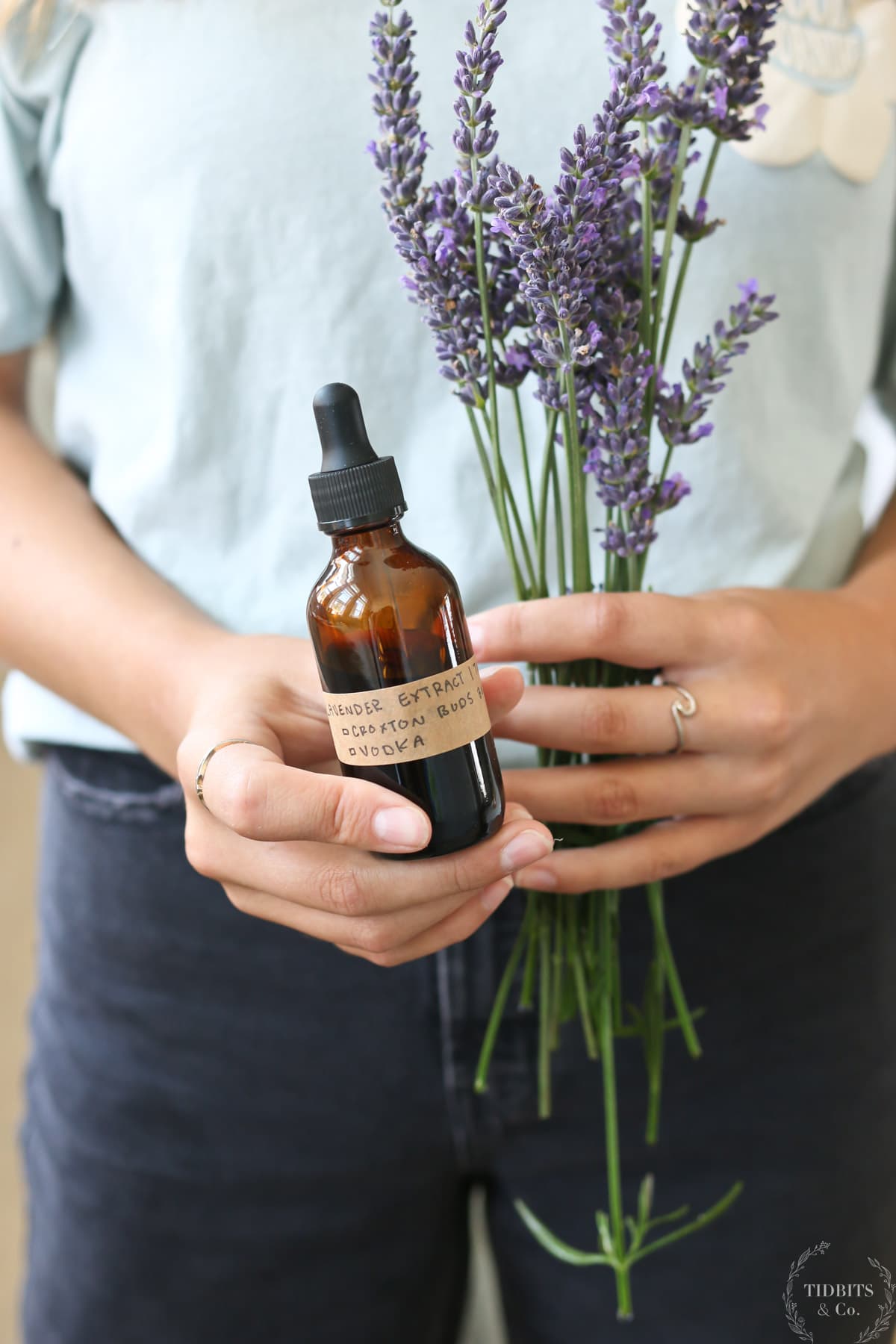 A girl holds a bottle of lavender extract and some lavender flowers