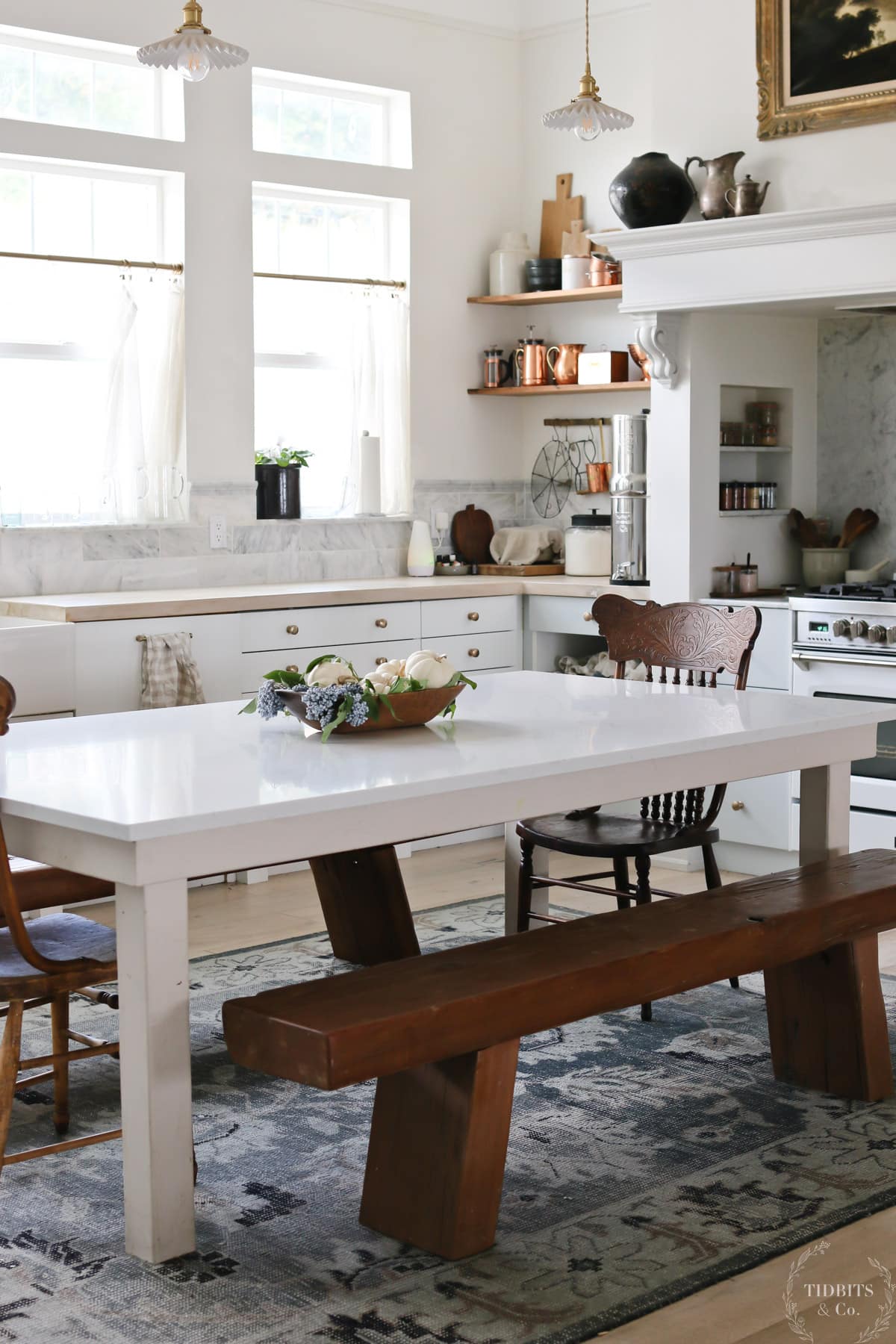 A country kitchen with cabinets, benches and a table with a fall floral arrangement