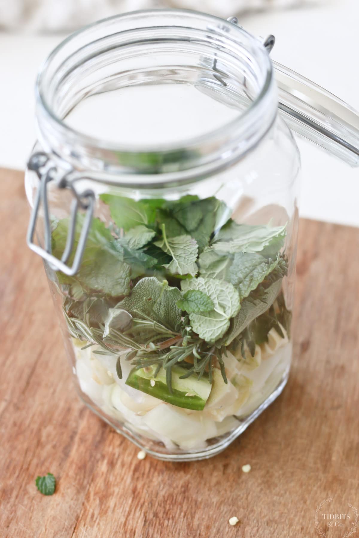A glass jar holds layers of vegetables and herbs