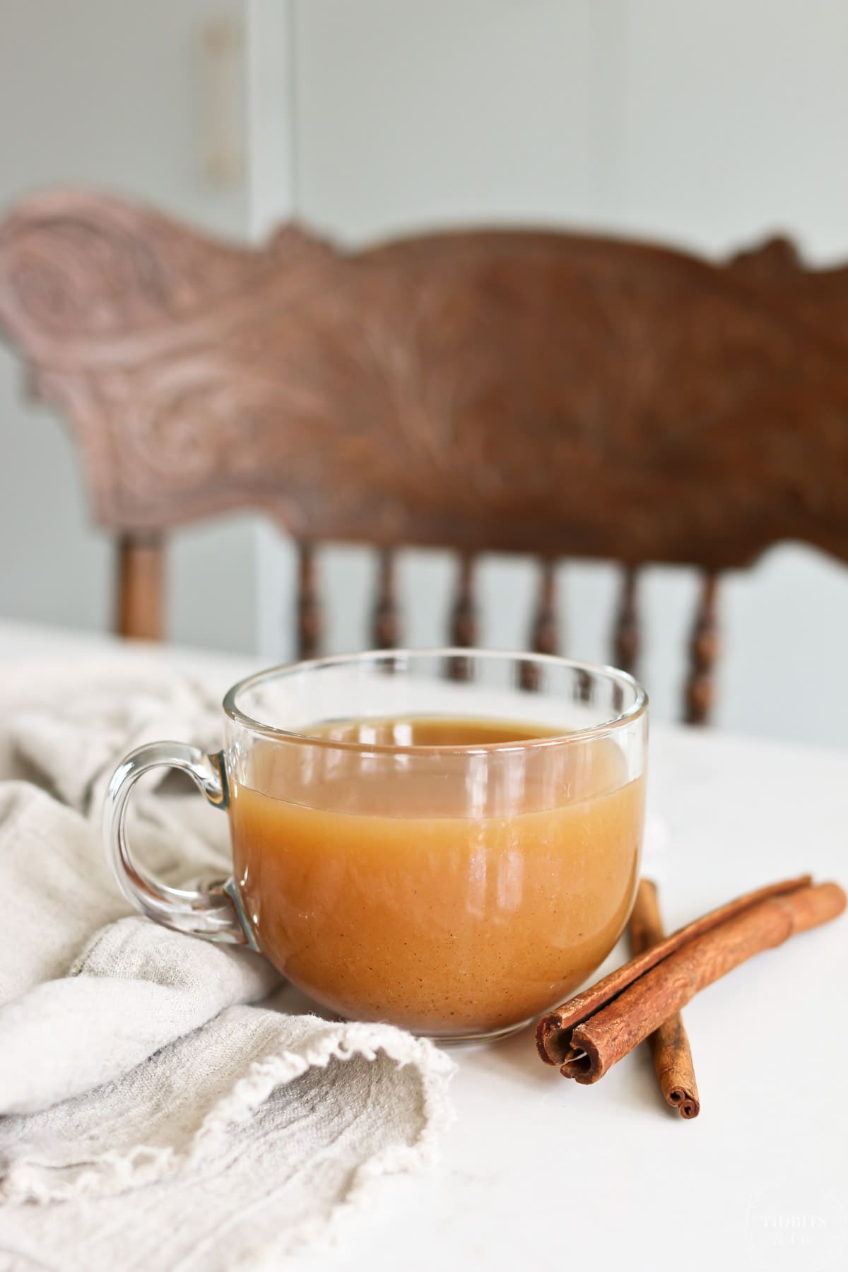 A glass cup of wassail sits next to two cinnamon sticks