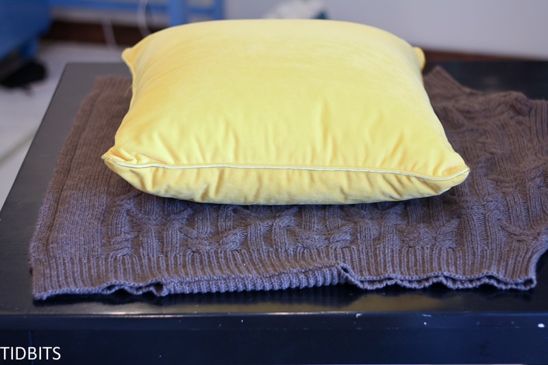 Yellow pillow sits on a gray sweater 