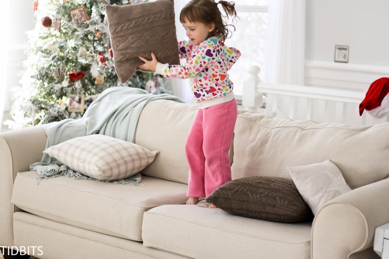Little girl standing on a couch holding a pillow