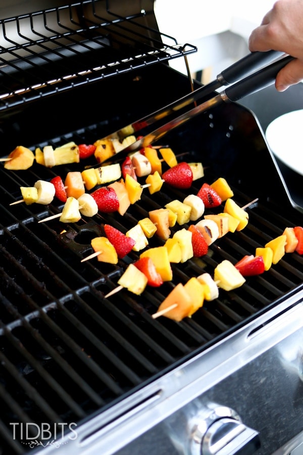 Flipping grilled fruit skewers on grill with a pair of tongs