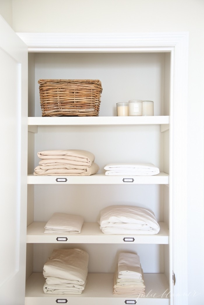 A cupboard holds folded linens, candles and a wicker basket