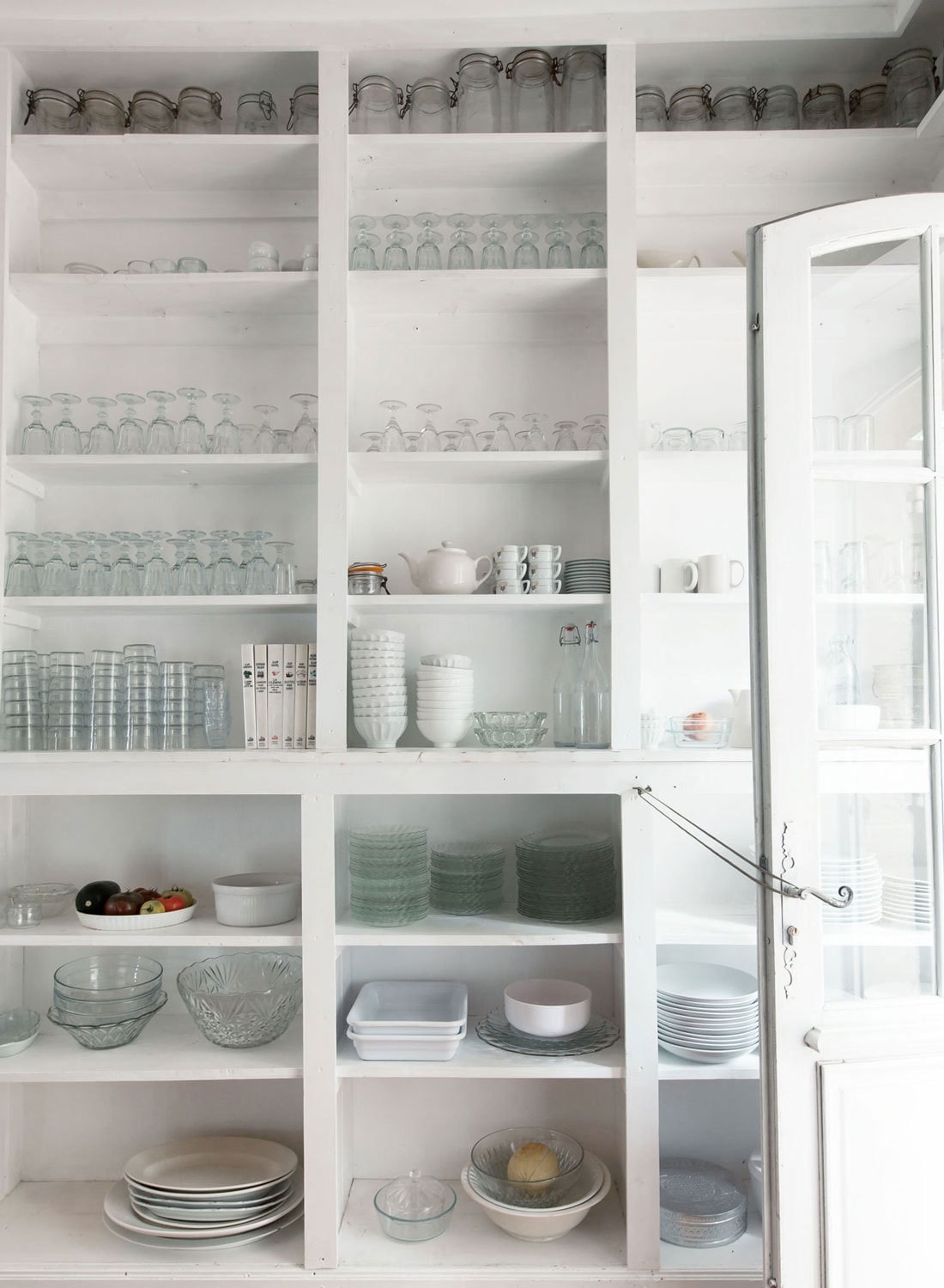 Kitchen shelves are stacked with beautifully organized glass jars, drinking glasses and assorted dishes