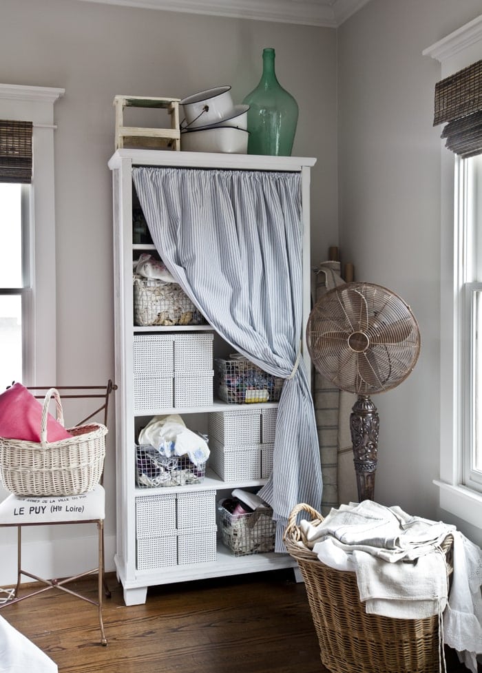 A bookcase with fabric totes and baskets is covered with a fabric curtain