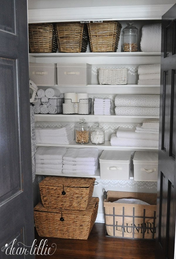 A linen closet is filled with folded towels, baskets and fabric totes