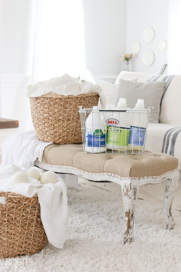 wooden laundry basket with white towels on top of living room sofa and a basket of laundry detergent