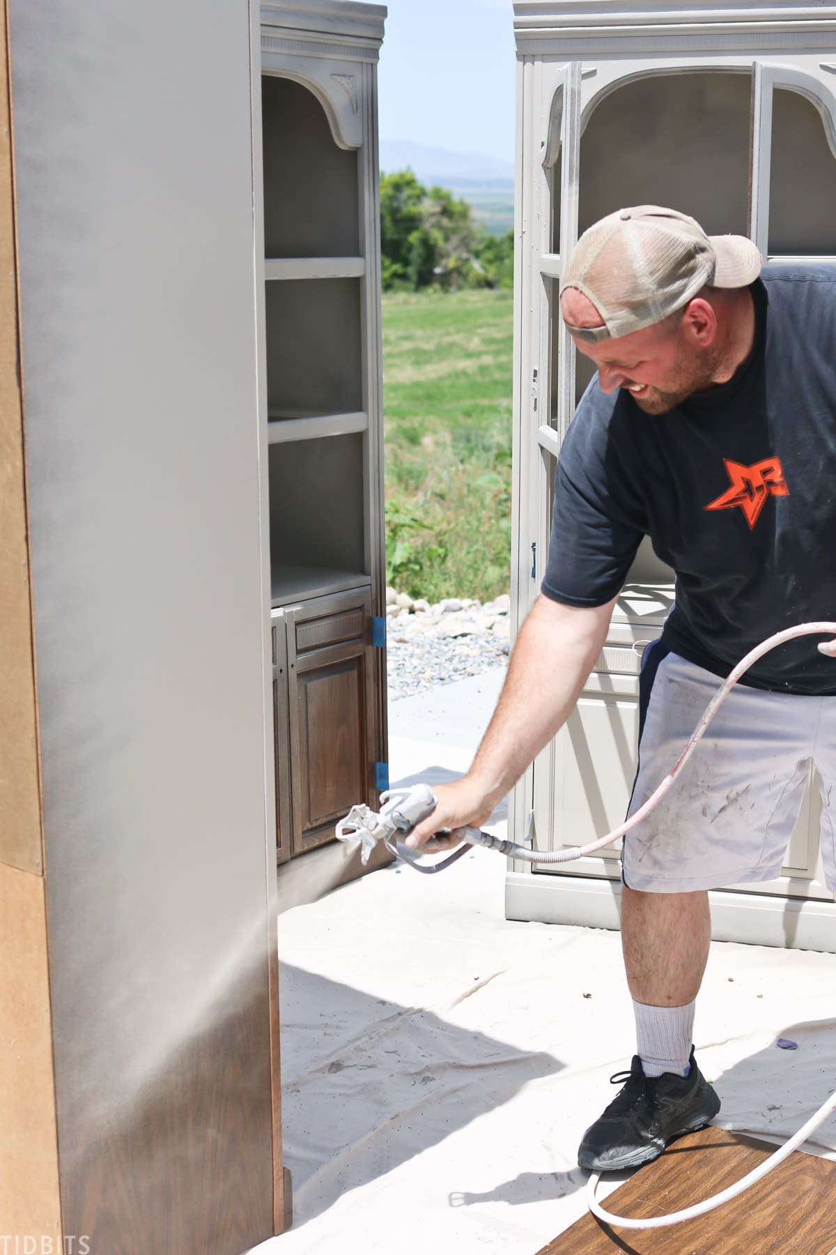 man spray painting old bookshelf with gray paint