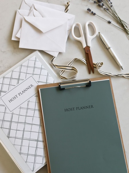The Host Planner binder placed next to scissors, ribbon, a pen, and envelopes