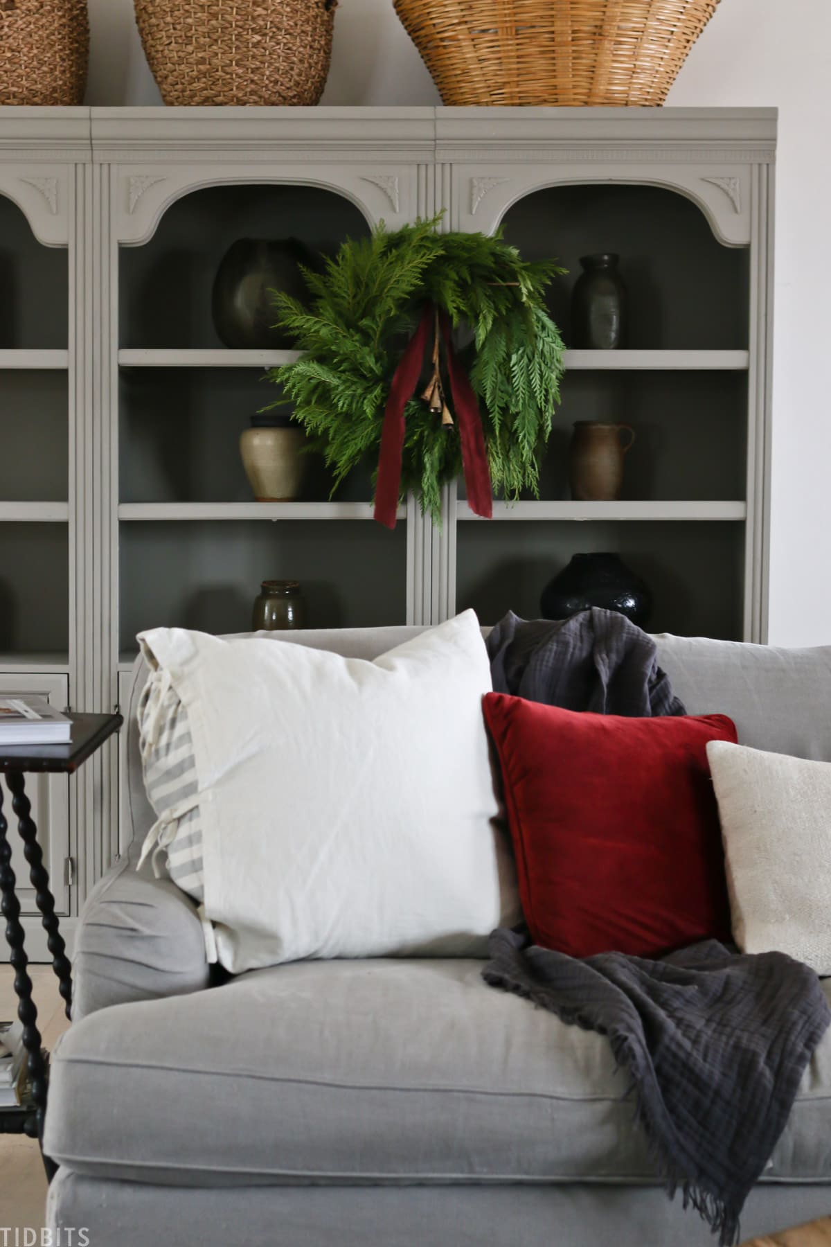 gray couch with decorative pillows with a Christmas wreath and red ribbon hanging above it