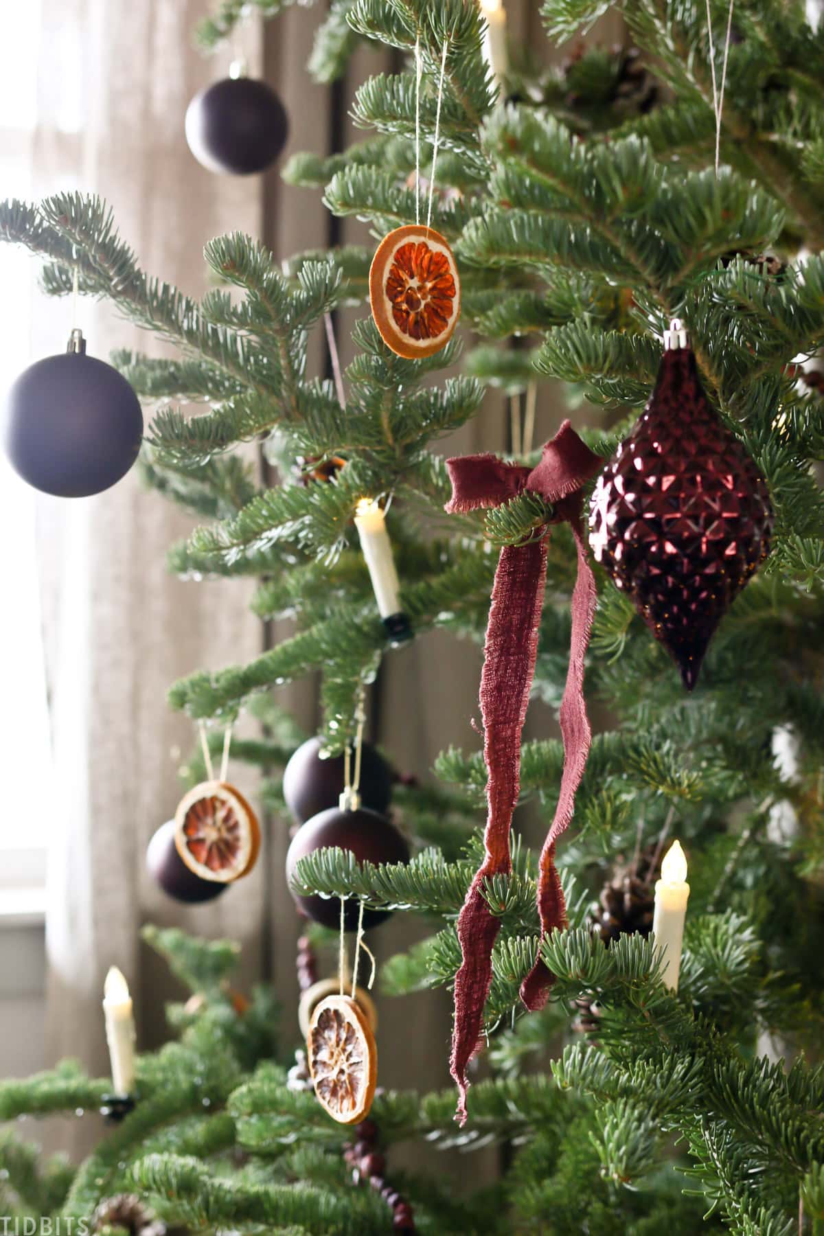 Christmas ornaments, candles and sliced oranges on a Christmas tree with a red linen ribbon