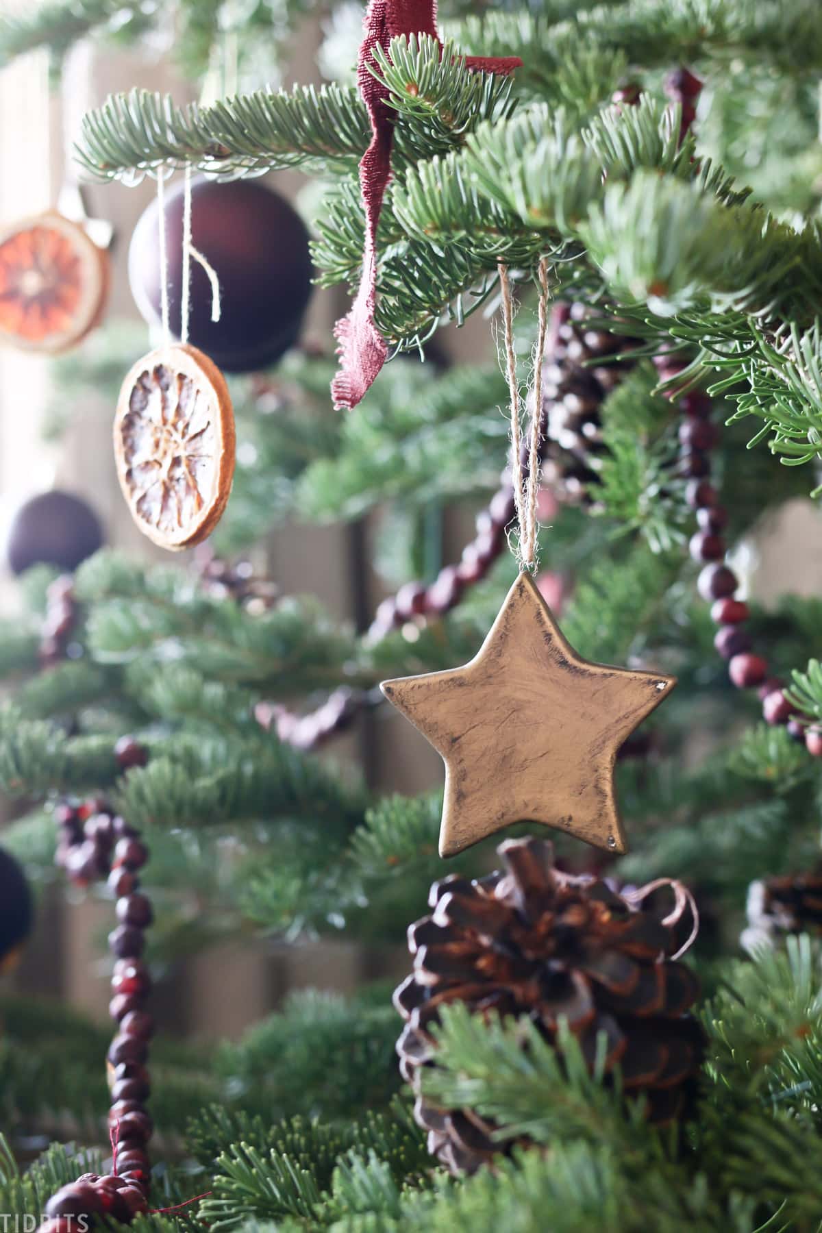 ceramic star hanging off Christmas tree branch next to round ornament and orange garland