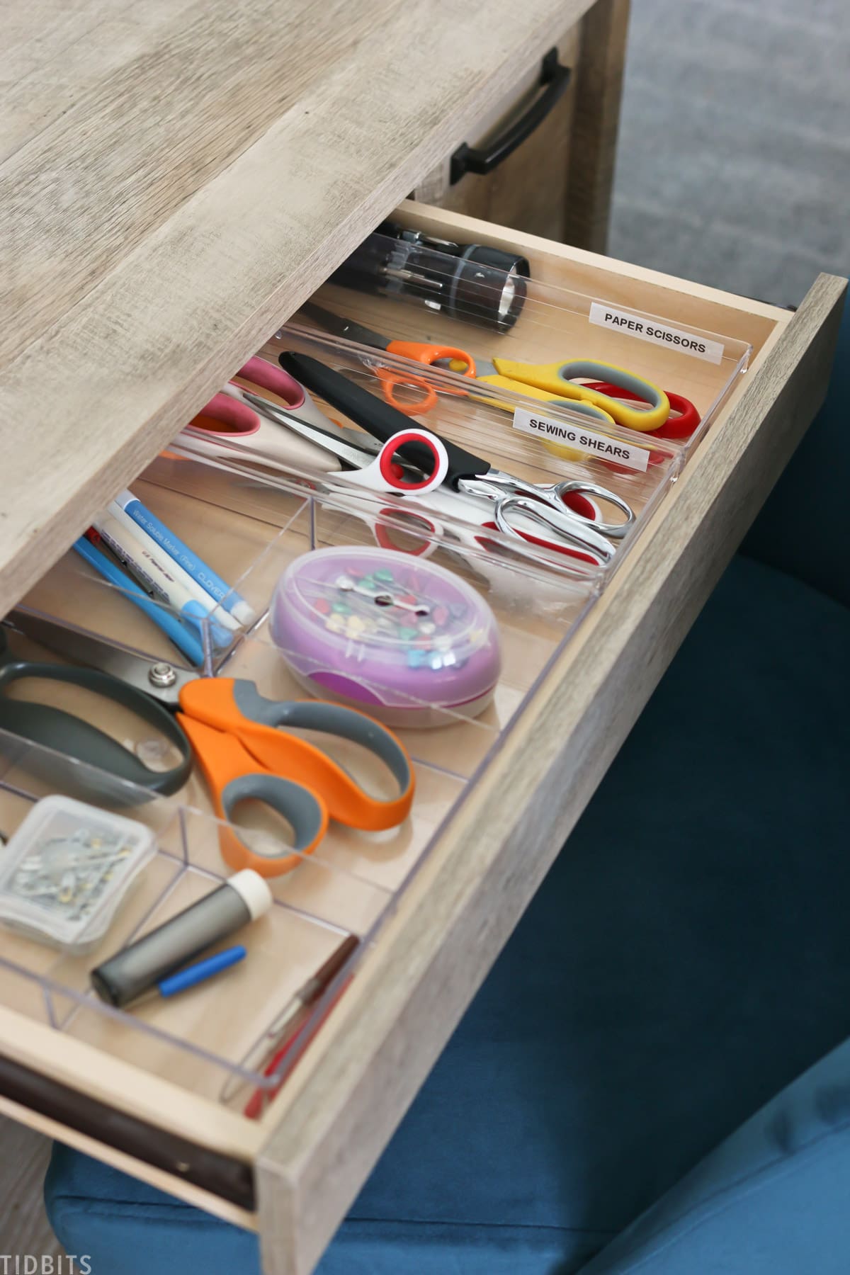 desk drawer is opened to show three containers organizing paper scissors, sewing shears, and sewing needles