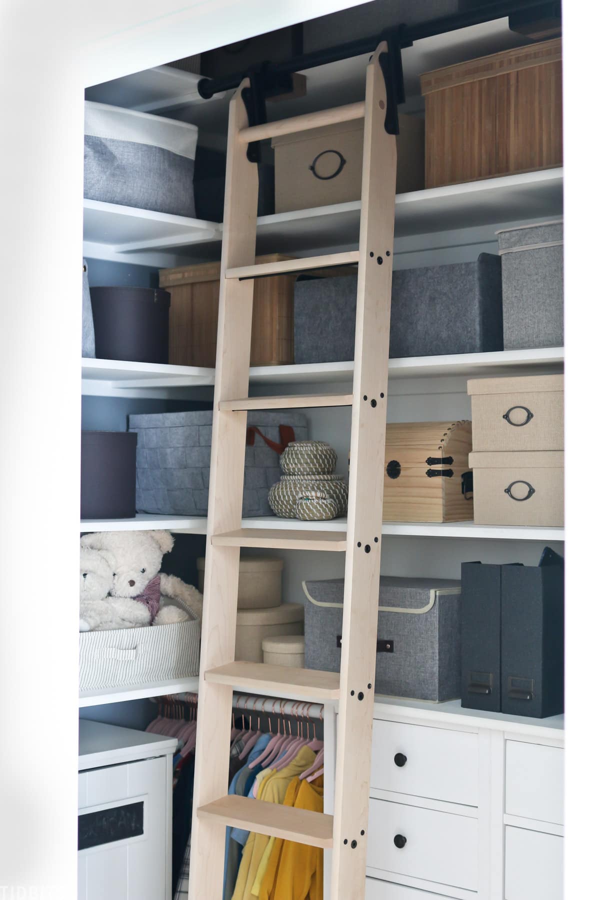 ladder inside of a kids closet with storage bins placed on built in shelves