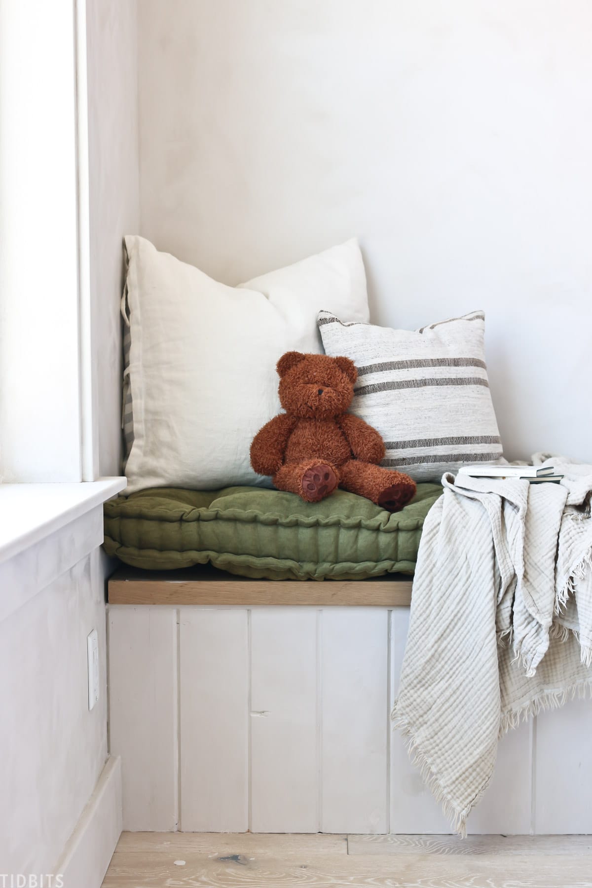 blanket hutch that has a teddy bear, pillows, and blanket on top of a bench cushion