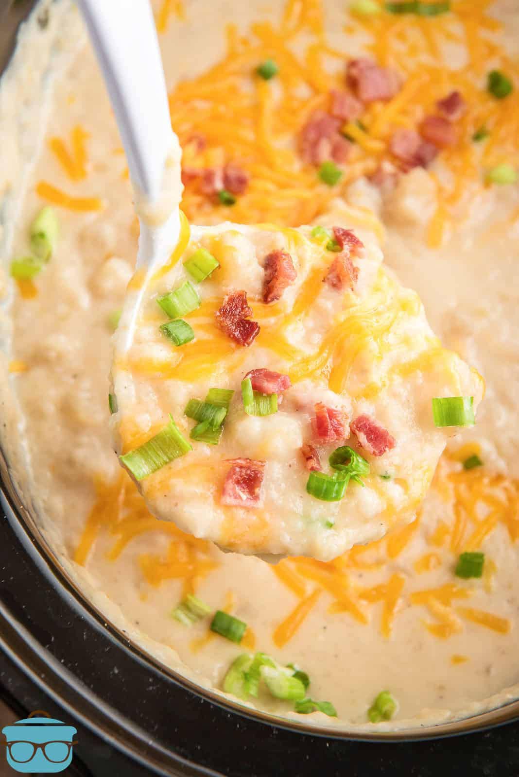 Close up of ladle scooping crockpot potato soup topped with cheese, bacon and green onions