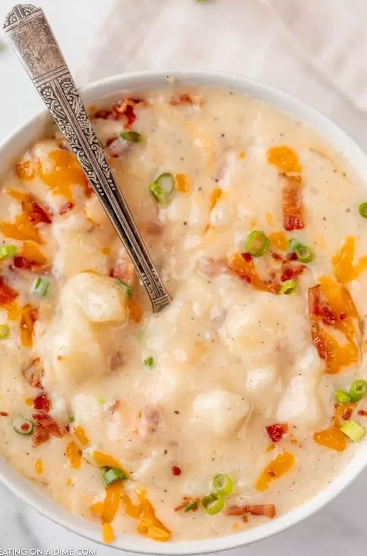 Crockpot potato soup recipe in bowl with cheese, bacon and green onion toppings