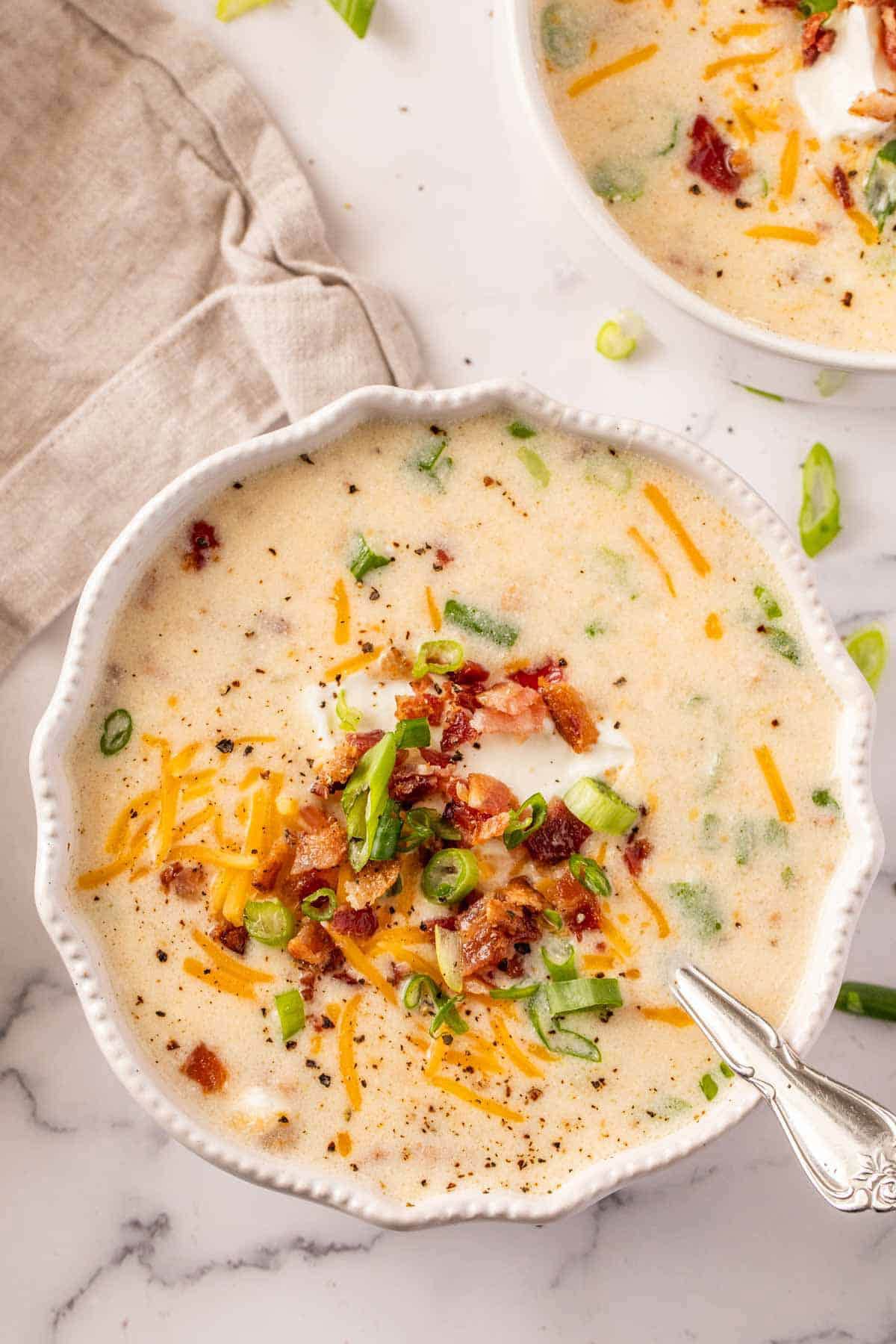 A bowl of crockpot potato soup with cheddar cheese, bacon, green onion and sour cream toppings