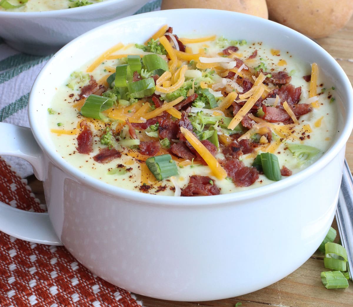 White cup full of loaded baked potato soup with cheese, green onion  and bacon toppings