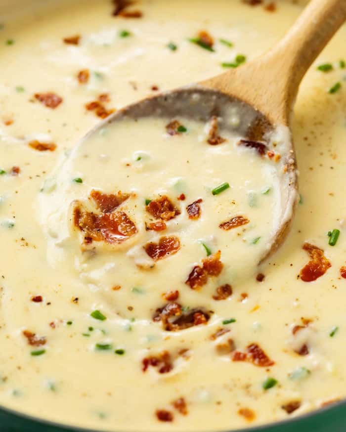 Wooden spoon in a bowl of silky potato soup topped with bacon and green onions