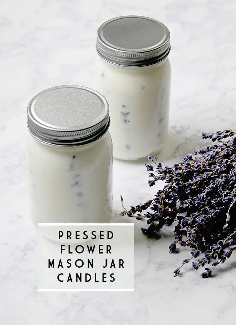 Two glass mason jar candles with pressed lavender flowers sit on a countertop