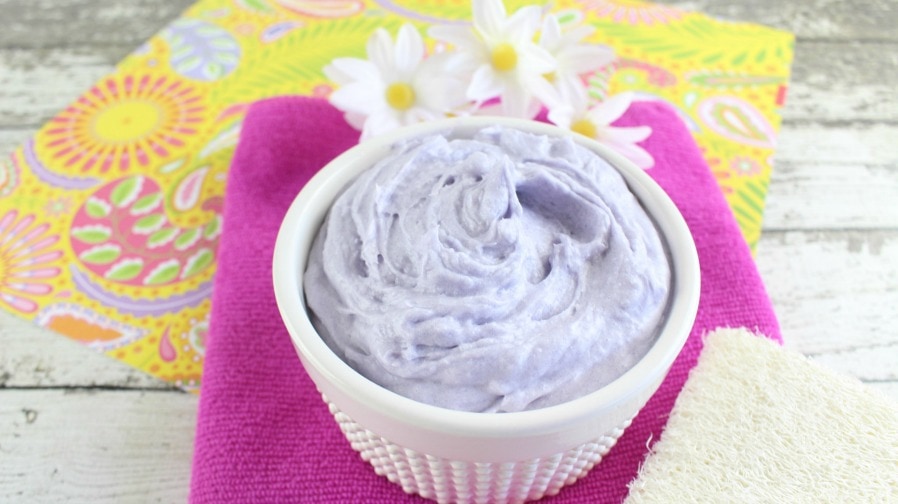 A bowl of DIY whipped lavender body butter sits on colorful towels