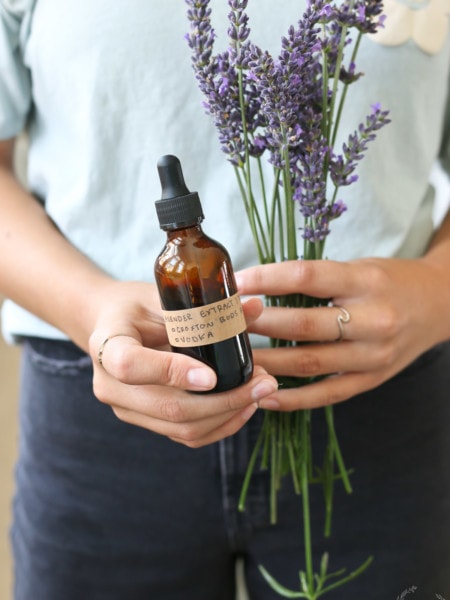 A girl holds a bottle of lavender extract and some lavender flowers