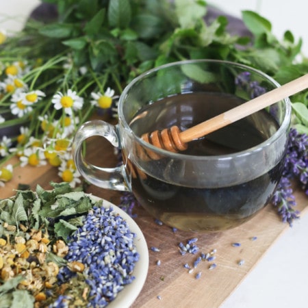 A cup of lavender tea sitting beside a mix of herbs