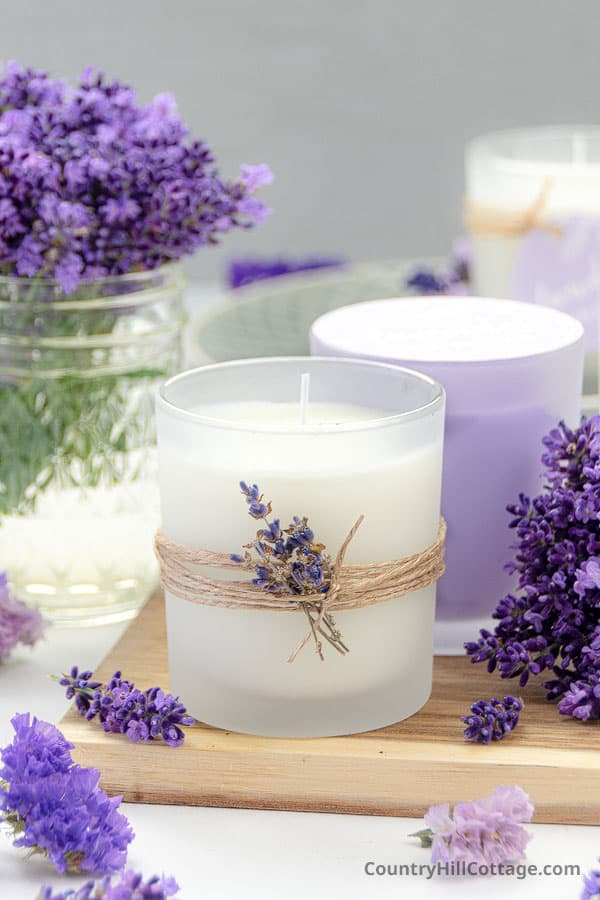 A lavender soy candle and lavender flowers sit on a cutting board