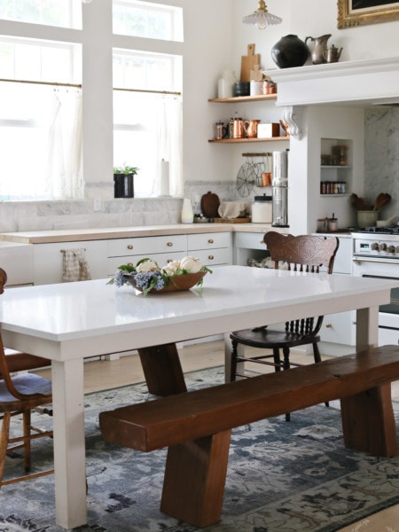 A country kitchen with cabinets, benches and a table with a fall floral arrangement