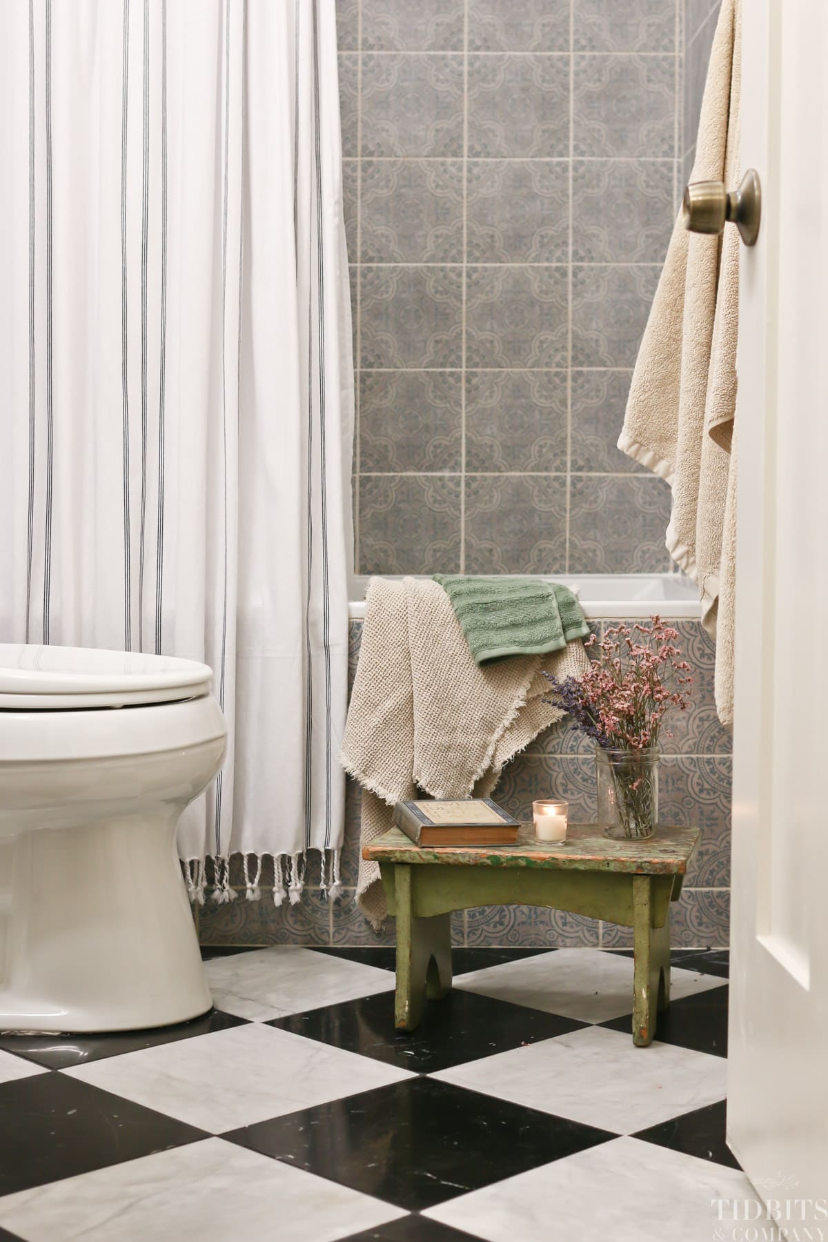 A remodeled split bathroom with marble tile floor, a stool, books, flowers and towels