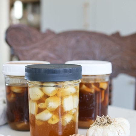 Three jars of fermented garlic infused honey sit on a table