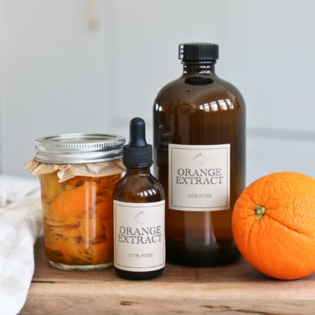 Glass bottles of extract sit next to oranges and a jar of orange extract