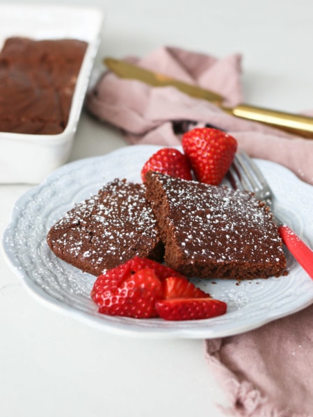 A while plate holds healthy cake like chocolate brownies and some sliced strawberries