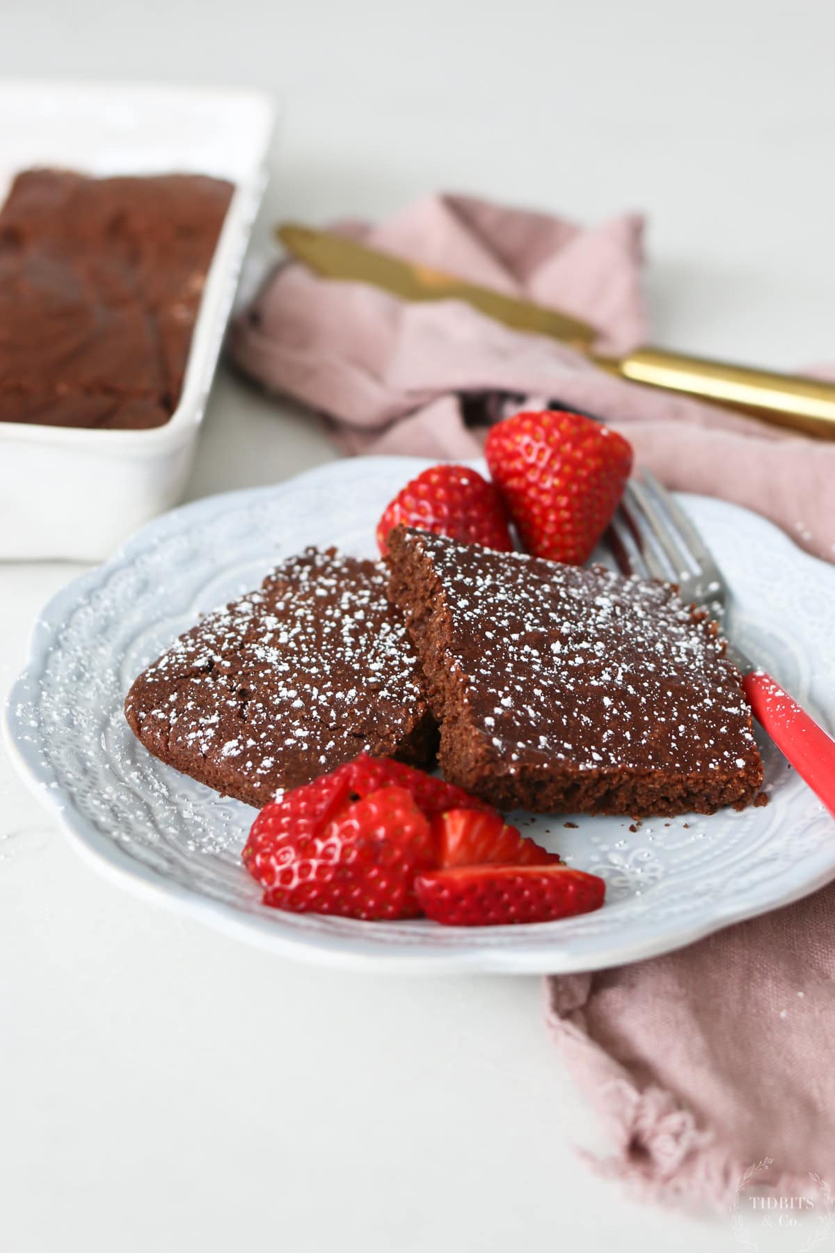 A while plate holds healthy cake like chocolate brownies and some sliced strawberries
