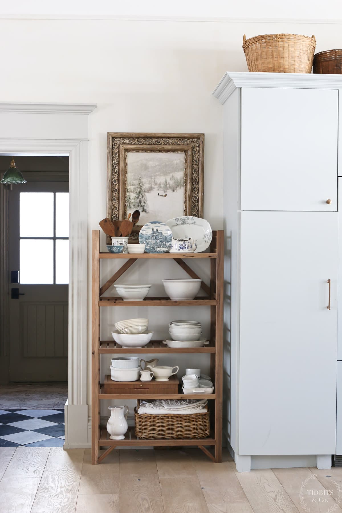 A baker's rack holds blue and white dishes below an piece of vintage art